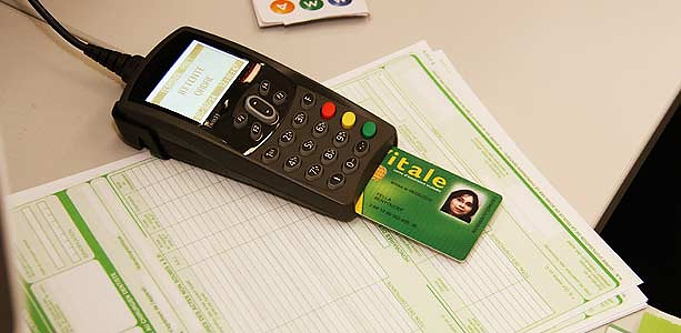Un terminal de paiement portable lit une carte Vitale verte posée sur des formulaires de feuilles de soins imprimés.
